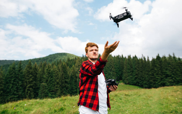 Jongeman video maker vliegt een drone in de bergen, lanceert een drone uit zijn handen. Reisinhoud maken van een drone - Foto, afbeelding