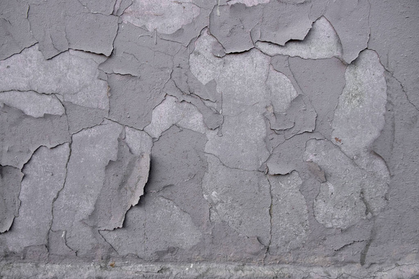 oude grijze schilferende verf op een betonnen muur met scheuren en krassen. ruwe oppervlaktestructuur - Foto, afbeelding