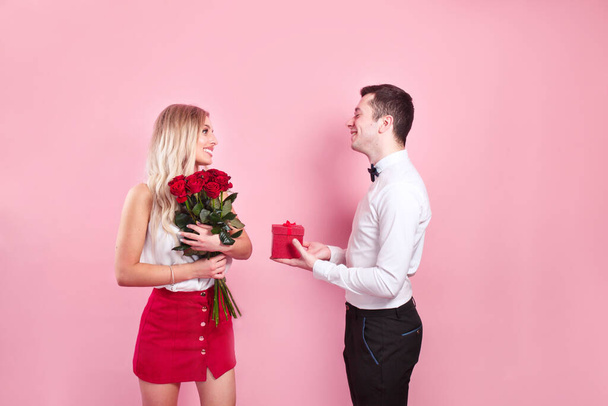 День святого Валентина. Красивий елегантний хлопчик пропонує своїй красивій дівчині своїми трояндами і посміхається
. - Фото, зображення