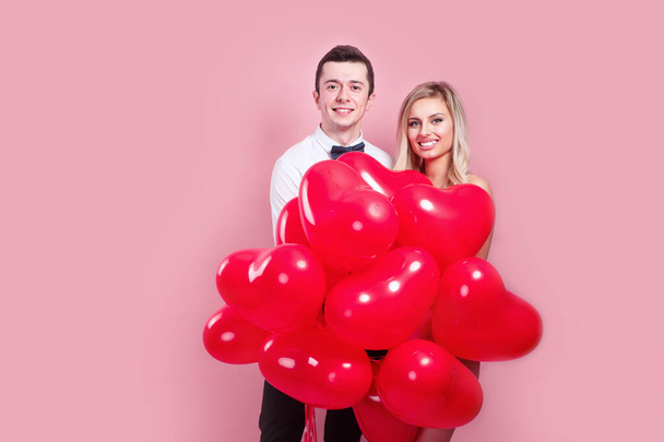 Valentines day. Happy young couple with heart shaped balloons on pink background. - Fotó, kép