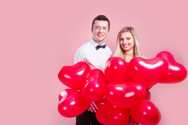 Valentines day. Happy young couple with heart shaped balloons on pink background. - Photo, image