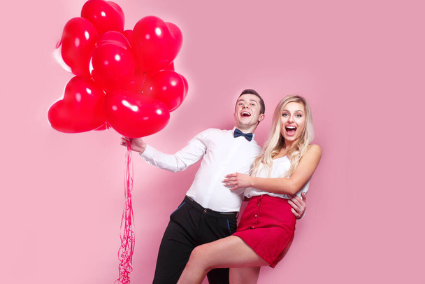 Valentines day. Happy young couple with heart shaped balloons on pink background. - Valokuva, kuva