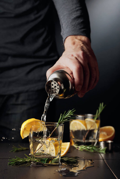 Cocktail Gin y Tonic con limón y romero. El camarero vierte un cóctel de una coctelera en un vaso. - Foto, Imagen