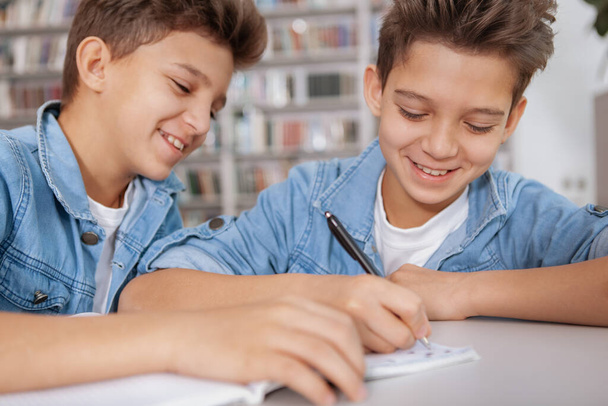 Cropped shot of two cheerful young boys enjoying studying together at the library. Happy twin brothers doing homework - 写真・画像