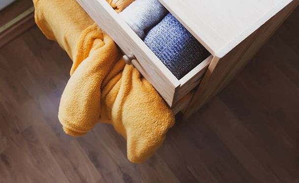 Ανοιχτή ξύλινη συρταριέρα με ζεστά πλεκτά μάλλινα ρούχα. Κατοικία κάθετη αποθήκευση. Οργάνωση ενδυμάτων. Μοντέρνα χρώματα. - Φωτογραφία, εικόνα