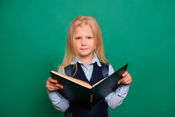 Κορίτσι στο σχολείο στολή με το βιβλίο στα χέρια απομονώνονται σε πράσινο φόντο. - Φωτογραφία, εικόνα