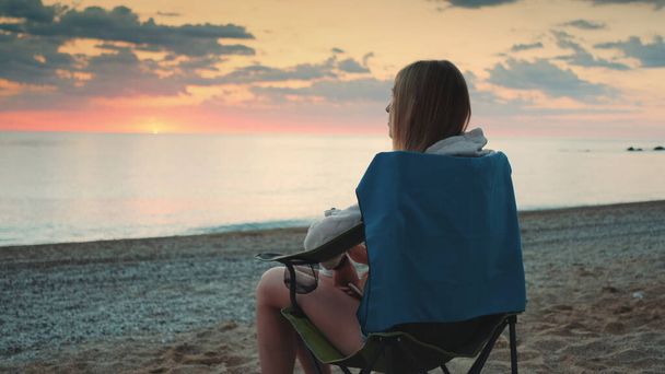Donna che beve dal thermos e si siede sulle sedie da campeggio sulla spiaggia - Foto, immagini