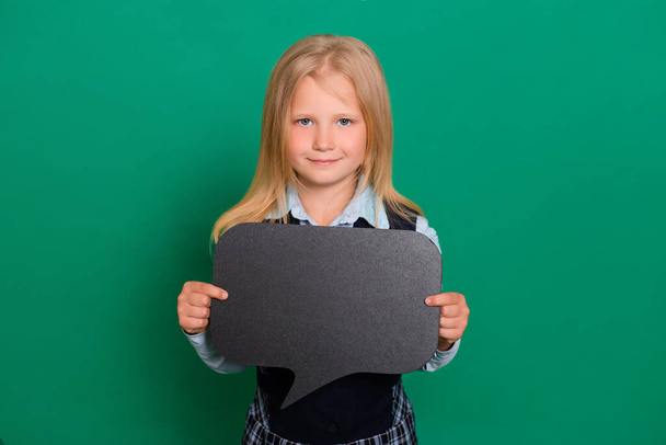 Little schoolgirl posing with a black board for inscriptions in hands isolated on a green background. Concept of idea, message. - Photo, Image