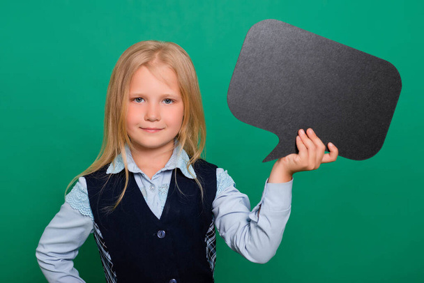 Little schoolgirl posing with a black board for inscriptions in hands isolated on a green background. Concept of idea, message. - Zdjęcie, obraz