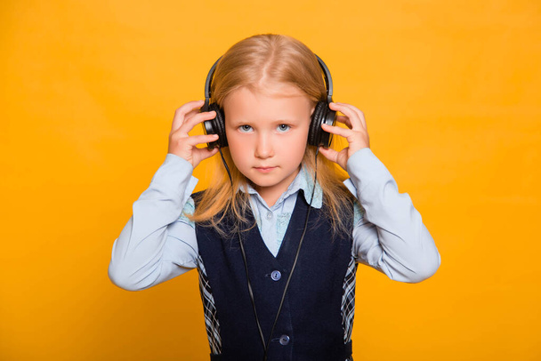 Little schoolgirl listens to music in headphones isolated on a yellow background. - Photo, Image