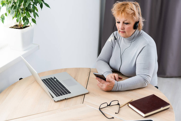 Χαμογελώντας σύγχρονη ώριμη 60s Καυκάσια γυναίκα στα ακουστικά παρακολουθούν webinar στο σπίτι. Ευτυχισμένη ηλικιωμένη γκριζομάλλα γυναίκα έχουν τη διασκέδαση μελέτη στο διαδίκτυο. Έννοια παλαιότερης τεχνολογίας - Φωτογραφία, εικόνα