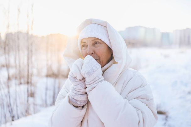 Glückliche ältere Seniorin in weißen warmen Outfits, die im sonnigen Winter draußen mit Schnee spielt. Gesunde Rentner im Urlaub Winteraktivitäten, aktives Lebensstil-Konzept - Foto, Bild