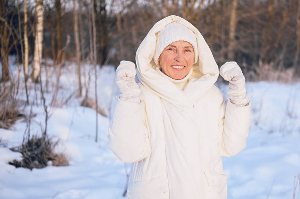 Счастливая пожилая пожилая зрелая женщина в белой теплой наружности играет со снегом в солнечную зиму на открытом воздухе. Отдыхающие здоровые люди отдых зимние мероприятия, концепция активного образа жизни - Фото, изображение