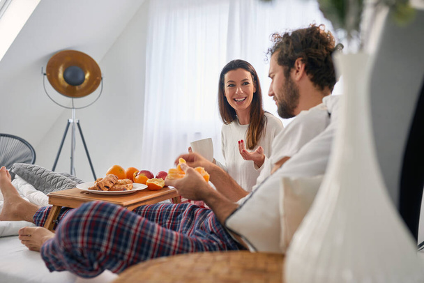 A young couple talking while eating delicious food for a breakfast in the bed at their bedroom. Love, relationship, together - Fotoğraf, Görsel