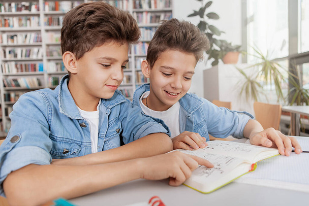 Two charming twin boys reading a book together at the library. School, education, friendship concept - Fotografie, Obrázek
