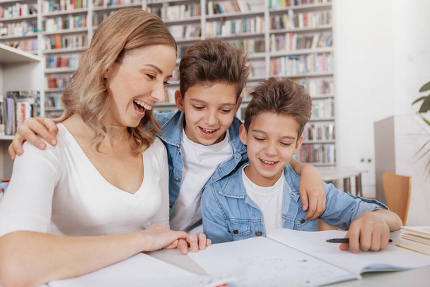 Excited woman laughing with her kids while helping them with homework at the library. Family, education concept - Foto, Imagen