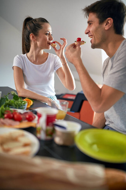 A young couple enjoying a breakfast in a cheerful atmosphere at home. Couple, home, togetherness, breakfast - Photo, Image