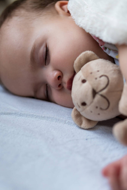 Childhood, care, motherhood, health concepts - Close up Little peace calm infant toddler baby girl sleep resting take deep nap laying hug teddy bear toy on soft warm blanket with close eyes on big bed - Photo, Image