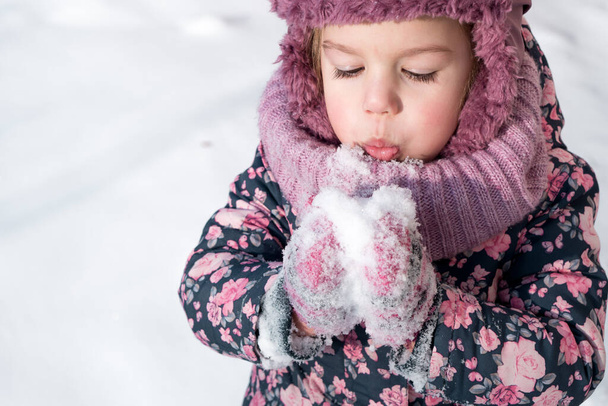Winter, games, family, childhood concepts - close-up portrait authentic little preschool minor girl in pink hat warm clothes have fun smiles in cold frosty weather day. Funny kid blow on white snow - Photo, Image