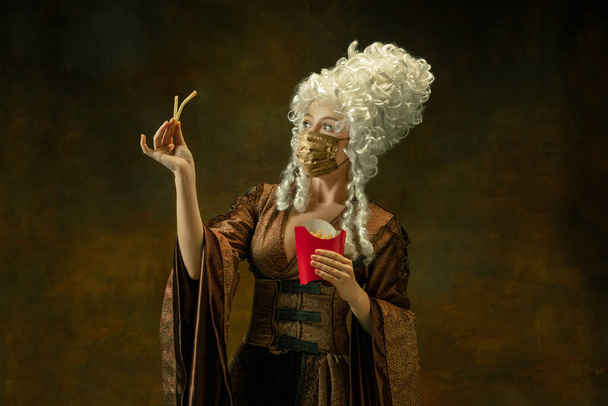 Portrait of medieval young woman in vintage clothes and golden face mask on dark background. - Photo, image