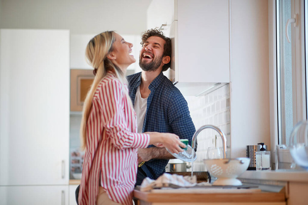 A happy couple having wonderful time while washing dishes in a cheerful atmosphere together. Kitchen, housework, home, relationship - Photo, image