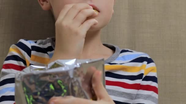 Malý chlapec sedí na pohovce, jí chipsy z balíčku - Záběry, video