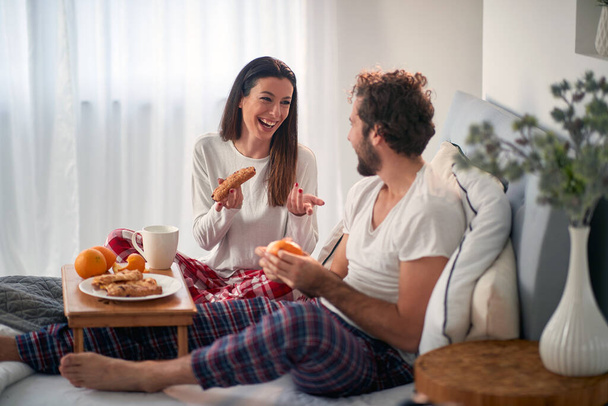 A young couple chatting while having a breakfast in the bed at their bedroom. Love, relationship, together - Foto, afbeelding