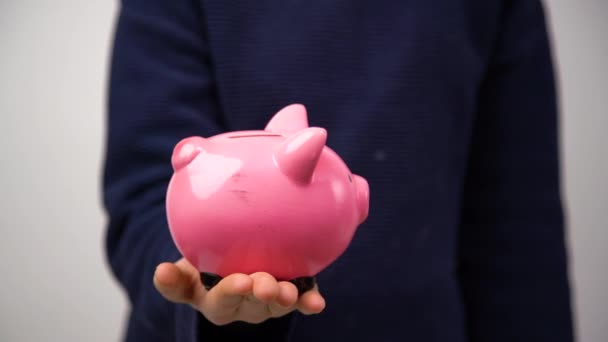 Großaufnahme eines jungen Unternehmers, der Münzen in ein Sparschwein steckt. Finanzielle Bildung für Kinder.  - Filmmaterial, Video