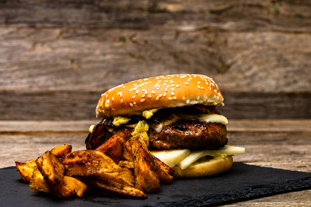 Házi készítésű, friss, ízletes sajtburger és sült krumpli egy fa asztalon. - Fotó, kép