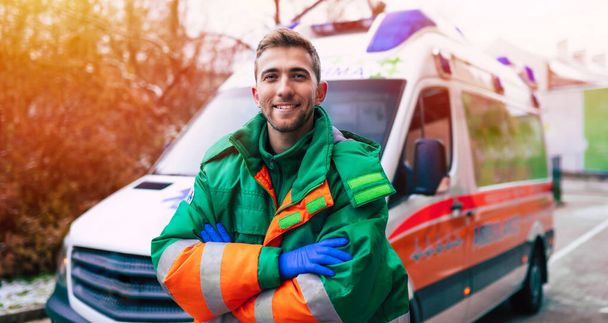 Professional and confident young man doctor looking on the camera with ambulance background - Photo, image