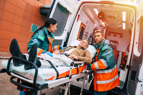 Serious and professional team of doctors in the ambulance moving on a patient into the hospital during an emergency situation. - Fotografie, Obrázek