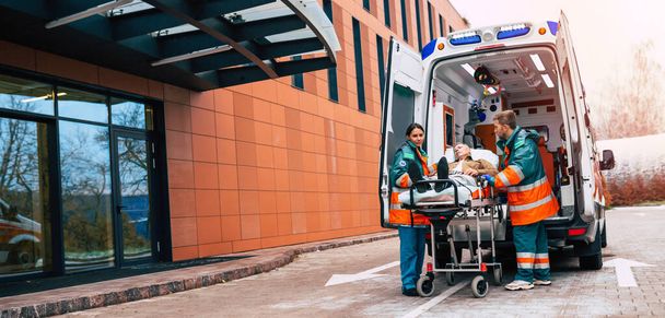 Serious and professional team of doctors in the ambulance moving on a patient into the hospital during an emergency situation. - Foto, Bild