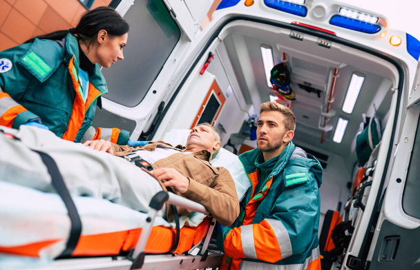 Serious and professional team of doctors in the ambulance moving on a patient into the hospital during an emergency situation. - Photo, Image
