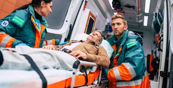 Serious and professional team of doctors in the ambulance moving on a patient into the hospital during an emergency situation. - Foto, afbeelding