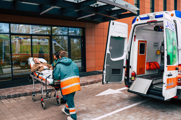 Serious and professional team of doctors in the ambulance moving on a patient into the hospital during an emergency situation. - Photo, image