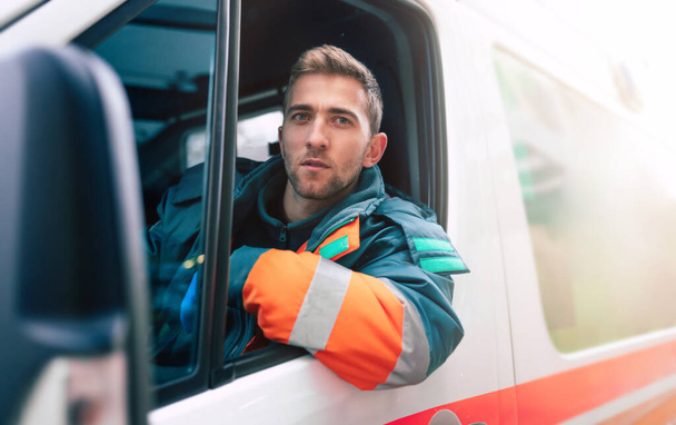 Professional and confident young man doctor looking on the camera with ambulance background - Foto, imagen