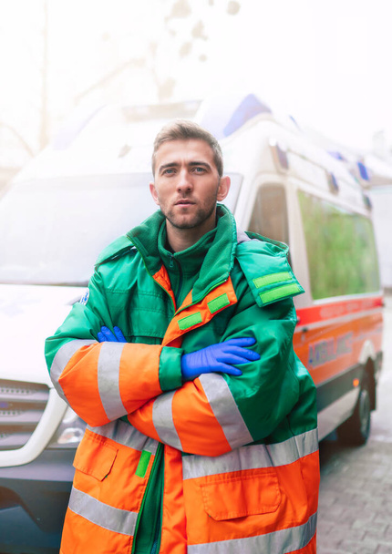 Professional and confident young man doctor looking on the camera with ambulance background - Foto, afbeelding