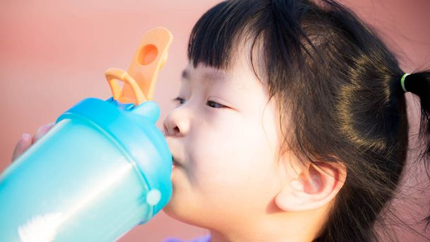 Κοντινό πλάνο του διψασμένου κοριτσιού που πίνει καθαρό νερό. Χαριτωμένο παιδί που κρατάει ένα μπλε μπουκάλι νερό. Υγιές παιδί με φρέσκο πρόσωπο μετά το πόσιμο νερό, ενώ ζεστή μέρα. Παιδική φροντίδα υγείας έννοια. Παγκόσμια ημέρα νερού. - Φωτογραφία, εικόνα