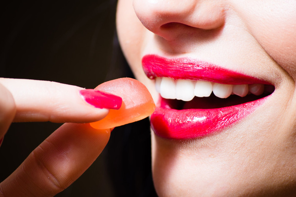 Seductive charming beautiful red lips and red color nails hand holding candy, closeup - Zdjęcie, obraz