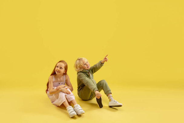 Childhood and dream about big and famous future. Boy and girl isolated on yellow studio background - Foto, Imagen