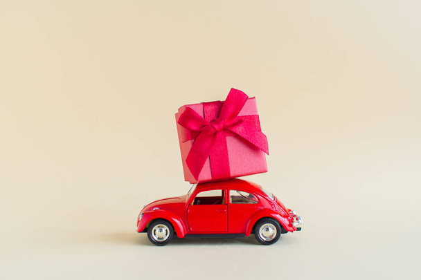 A miniature red car carrying a big gift. Holiday Valentines Day gifts, womens day, March 8, shopping. - Fotoğraf, Görsel