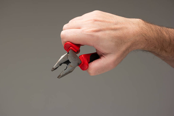 Caucasian male hand holding a metal plier with red plastic handles isolated on gray background. - Foto, immagini