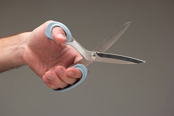 Blanke mannelijke hand met een speciale schaar gemaakt voor linkshandige mensen geïsoleerd op grijze achtergrond. - Foto, afbeelding
