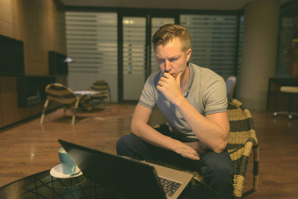 Portrait of young handsome man using laptop in the living room - Foto, afbeelding