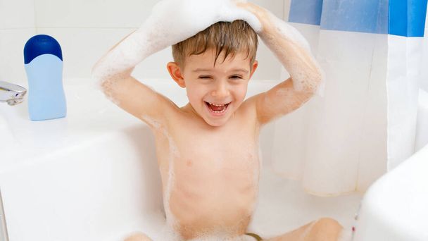 Joyeux petit garçon drôle se lavant la tête avec un shampooing tout en prenant un bain à la maison. Concept d'hygiène infantile et de soins de santé à domicile. Les enfants s'amusent et jouent - Photo, image