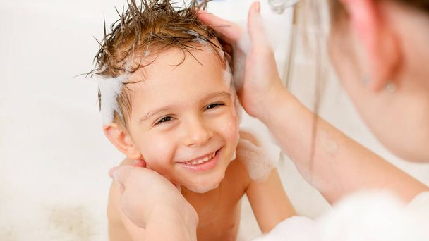 Portret van schattig glimlachend jongetje met moeder wassen in bad - Foto, afbeelding