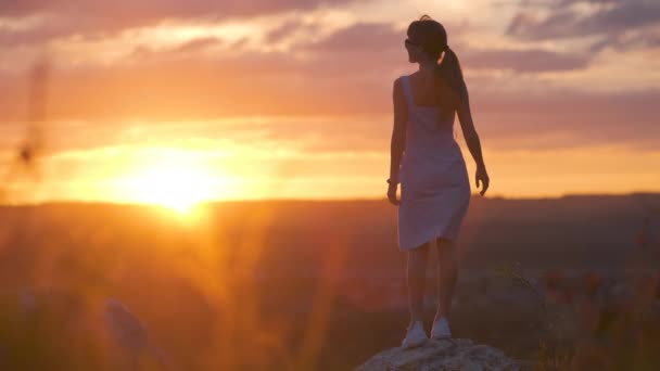 Silhueta escura de uma jovem mulher em vestido de verão em pé ao ar livre desfrutando de vista da natureza ao pôr do sol. - Filmagem, Vídeo