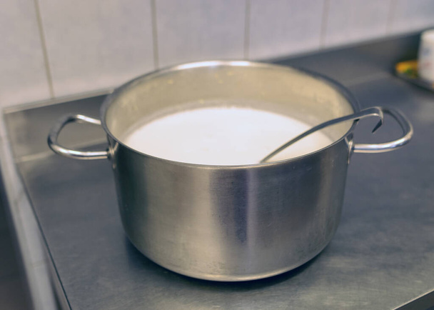 olla de metal con taza en la tapa de la estufa con sopa de leche, cocina de la escuela, comer concepto de cocina, olla de cocina de metal - Foto, imagen