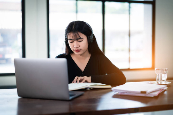 Hymyilevä aasialainen tyttö opiskelija käyttää langattomia kuulokkeita kirjoittaa muistikirjaan opiskella kieltä verkossa katsella ja kuunnella luennoitsija, webinar kautta videopuhelu verkko-oppimista kotona, etäopetus - Valokuva, kuva