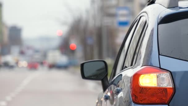 Close-up van de achterlamp van een kapotte auto geparkeerd aan een straatkant van de stad met knipperende signaallichten. - Video